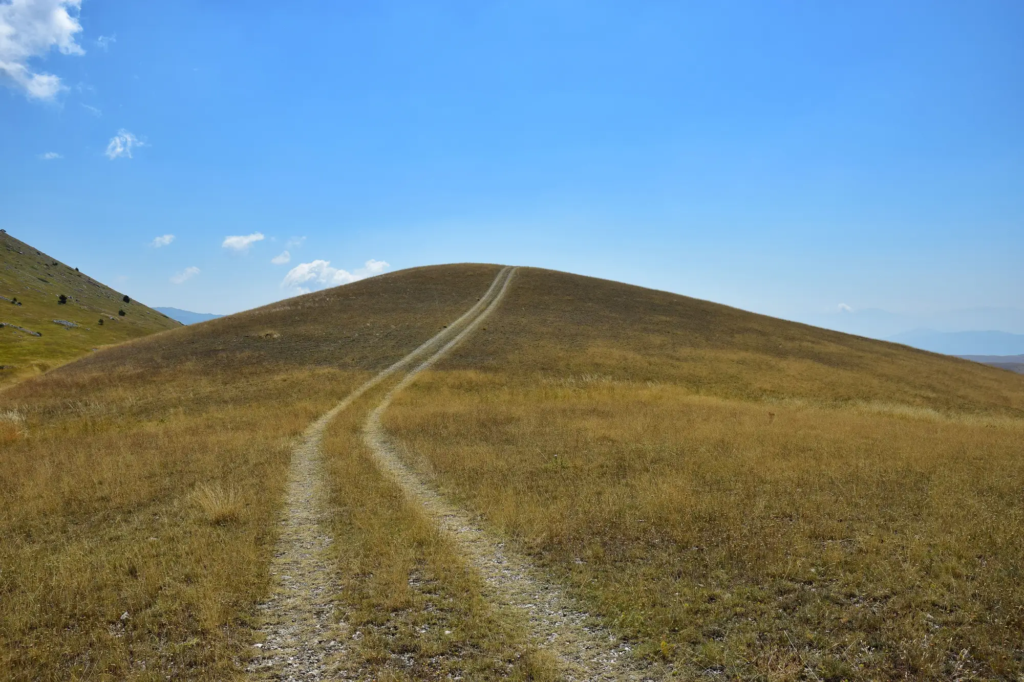 A dry, grassed dome with a two-rut track running up and over its crown under a clear sky